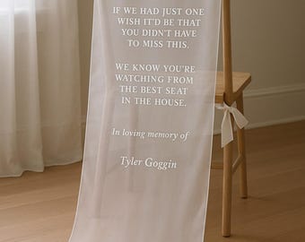 May include: A sheer white fabric chair sash with printed text. The text reads "IF WE HAD JUST ONE WISH IT'D BE THAT YOU DIDN'T HAVE TO MISS THIS. WE KNOW YOU'RE WATCHING FROM THE BEST SEAT IN THE HOUSE. In loving memory of Tyler Goggin."