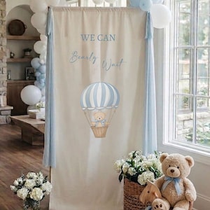 May include: A tall rectangular fabric backdrop in cream featuring the blue text WE CAN Bearly Wait and a graphic of a teddy bear in a blue and white striped hot air balloon, accented with light blue and white balloons on the top corners.