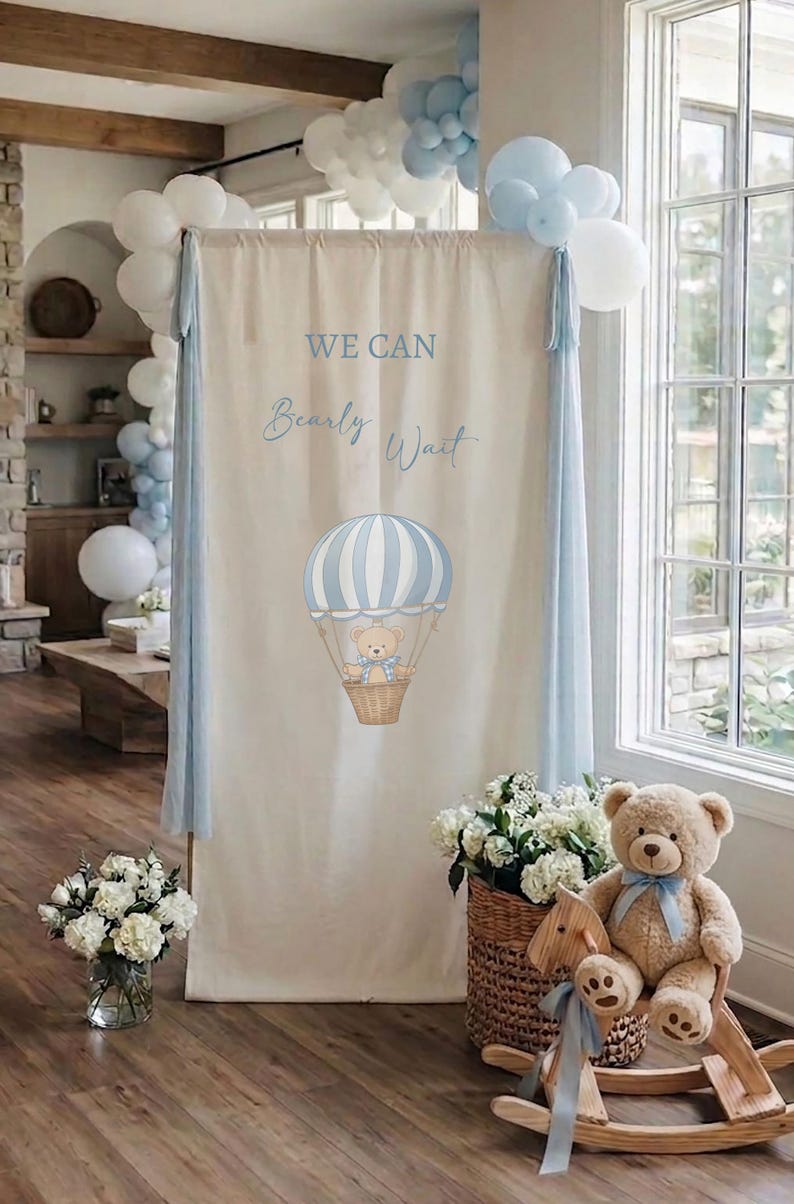 May include: A tall rectangular fabric backdrop in cream featuring the blue text WE CAN Bearly Wait and a graphic of a teddy bear in a blue and white striped hot air balloon, accented with light blue and white balloons on the top corners.