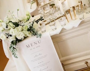 Könnte beinhalten: Eine weiße Leinen-Speisekarte mit schwarzem Text für einen Hochzeitsempfang. Die Speisekarte listet die Vorspeise, das Hauptgericht und das Dessert auf. Der Text oben lautet "MENU 12.12.2023". Am unteren Rand der Speisekarte steht "Olivia & Michael".