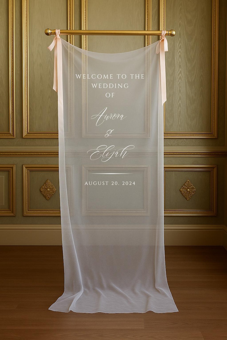 May include: A sheer white wedding welcome sign with the text "WELCOME TO THE WEDDING OF Aurora & Elijah AUGUST 20, 2024". The sign is suspended from a gold rod with pink ribbons.