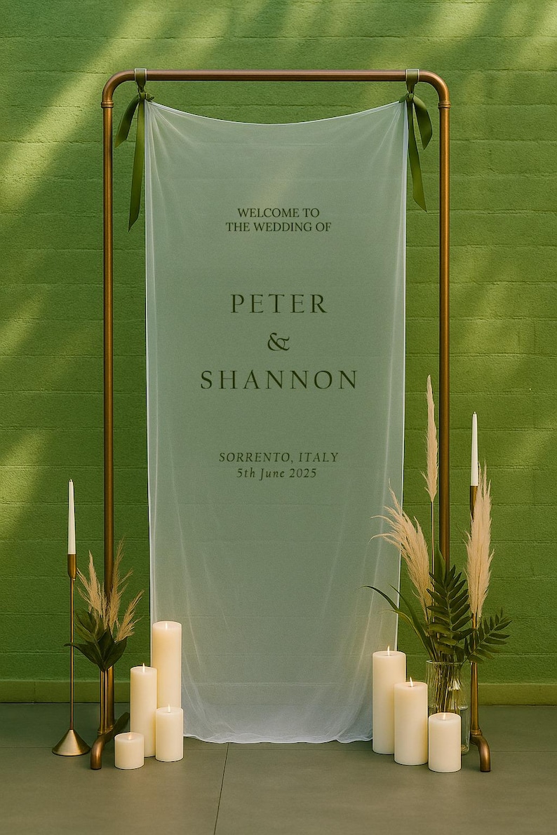 May include: Wedding sign with the text "Welcome to the Wedding of Peter & Shannon" and the date "5th June 2025" in Sorrento, Italy. The sign is draped with sheer fabric and framed by a gold metal structure. Candles and floral arrangements are at the base.