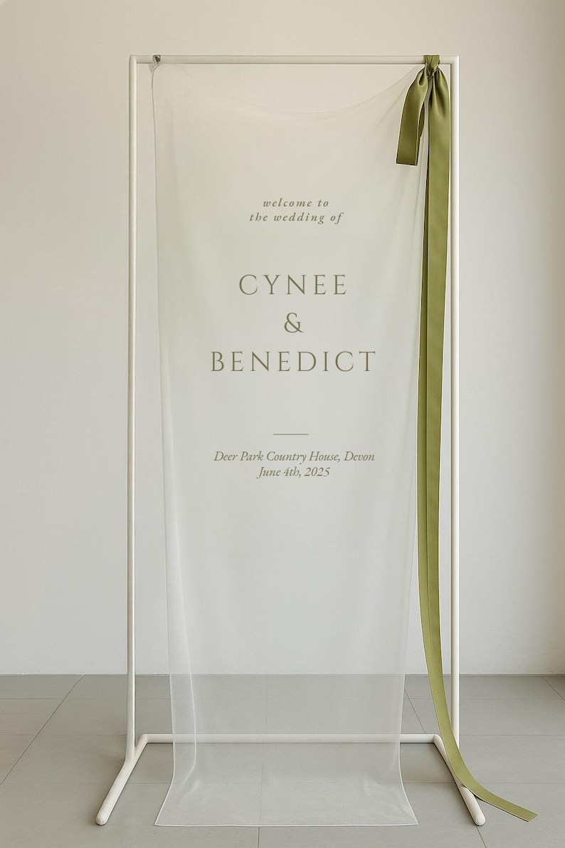 May include: A white wedding welcome sign with the names "CYNEE & BENEDICT" in a soft green font. The sign includes the wedding date and location, with a green ribbon accent. The sign is displayed on a white metal frame.