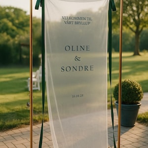 May include: A wedding sign with a sheer white fabric banner suspended from a gold metal frame. The banner has dark green ribbons and features the names "Oline & Sondre" and the date "16.08.25" in black text. The sign is outdoors.