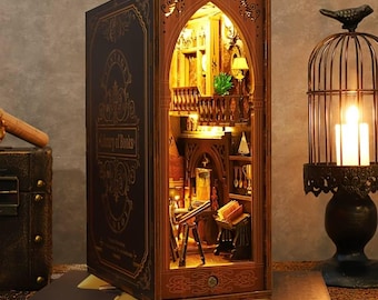 May include: A wooden miniature library diorama with warm interior lighting. The exterior is designed to resemble a large book with the words "Library of Books" in gold lettering. The interior features a detailed library scene with miniature furniture and decor.