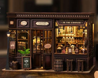 May include: A miniature wooden tavern model with intricate details. The model features a bar, shelves stocked with bottles, and a sign that reads "The Hidden Tavern in the Corner." The exterior includes a "Wine Shop" sign and a street lamp.