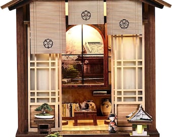 May include: Miniature Japanese-style wooden house with a detailed interior. Features include a bonsai tree, a small table with books and pottery, and a traditional Japanese doll. The house has a stone base and a small stone lantern.