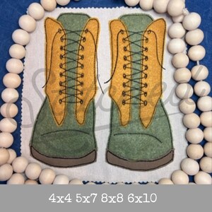 Puede incluir: Dos botas de fieltro verde con tapas de fieltro amarillo y costuras negras. Las botas tienen cordones que están atados en un patrón de cruz.