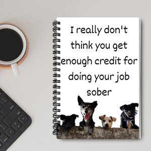 May include: A white spiral bound notebook with a black and white image of four dogs looking over a wall. The text on the notebook reads "I really don't think you get enough credit for doing your job sober."