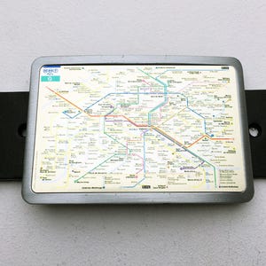 Può includere: Una mappa del sistema metropolitano di Parigi in metallo argentato con sfondo bianco e linee colorate che rappresentano le diverse linee. La mappa è circondata da una cornice argentata.