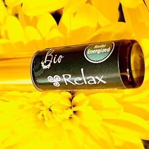 May include: A gold and black roller bottle with a label that says "Bio Relax" and "Reiki Energized". The bottle is sitting on a bed of yellow flowers.