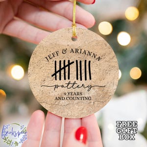 May include: A round, brown, textured ornament with the text "JEFF & ARIANNA pottery 9 YEARS AND COUNTING" and tally marks representing nine years.
