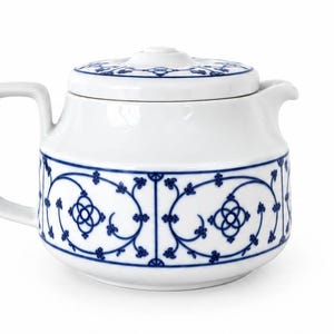 Könnte beinhalten: Eine weiße Teekanne aus Keramik mit einem blauen Dekor aus sich wiederholenden Blumenranken und geometrischen Formen auf dem Körper und dem Deckel. Die Teekanne hat einen quadratischen Griff, einen kurzen Ausguss und einen passenden Deckel.