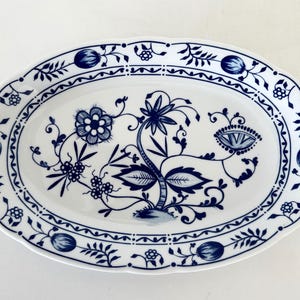 Könnte beinhalten: Ovale Servierplatte aus weißer Keramik mit blauem Blumenmuster. Die Platte hat einen gewellten Rand und ein detailliertes Muster aus Blumen, Blättern und dekorativen Bordüren. Ein klassisches Stück zum Servieren von Speisen.