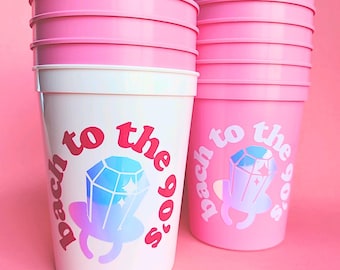 May include: Pink plastic cups with a white band around the middle. The cups have a graphic of a diamond ring with the text "back to the 90's" on them.