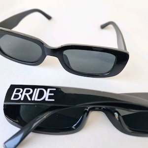 May include: Two pairs of black sunglasses. One pair has the word "BRIDE" written in white letters on the front.
