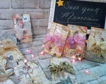 Puede incluir: Una colección de ocho sobres decorativos con papel vintage, adornos y cintas. Los sobres están decorados con mariposas, flores y otros diseños vintage. Los sobres están dispuestos en una fila sobre una superficie blanca con un cartel que dice "Save Your Memories".