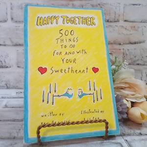 May include: A yellow and blue book titled "Happy Together 500 Things To Do For And With Your Sweetheart" with a red heart on each side of the title. The book is illustrated with a simple drawing of two people holding hands with swords in the background.