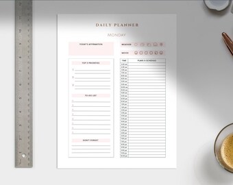 Puede incluir: Una hoja de planificador diario blanca con texto y acentos en oro rosa. El planificador incluye secciones para afirmaciones, clima, estado de ánimo, principales prioridades, lista de tareas y un horario. También se ven una regla de metal, un bolígrafo y una taza de café.