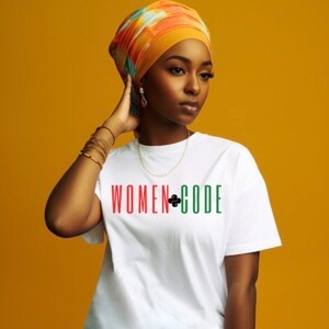 Peut inclure: Un t-shirt blanc avec le texte "WOMEN+CODE" en lettres rouges, vertes et noires. La personne portant le t-shirt porte un turban color&eacute;.