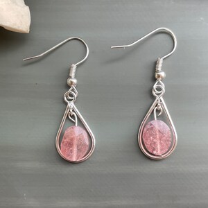 May include: A pair of silver dangle earrings with pink teardrop-shaped stones.