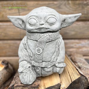 Może przedstawiać: Szara betonowa figurka ogrodowa przedstawiająca postać w szaliku i płaszczu. Figurka jest w stylu popularnej postaci fikcyjnej. Garden Ornaments by Onefold.