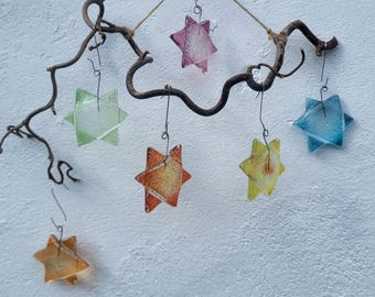 May include: A decorative wall hanging featuring a dark brown, twisted natural branch. Six translucent, multi-colored glass stars in shades of pink, green, orange, yellow, and blue are suspended from the branch by thin metal wires.