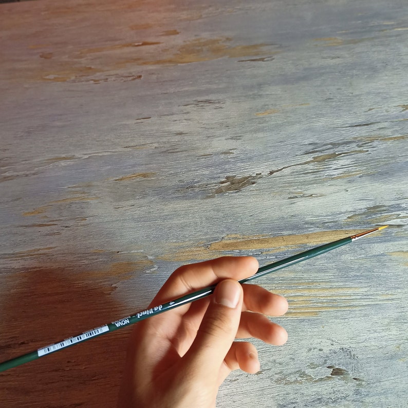 May include: A hand holds a green paint brush with a gold tip. The brush has a black label with the text "da Vinci NOVA" on it.