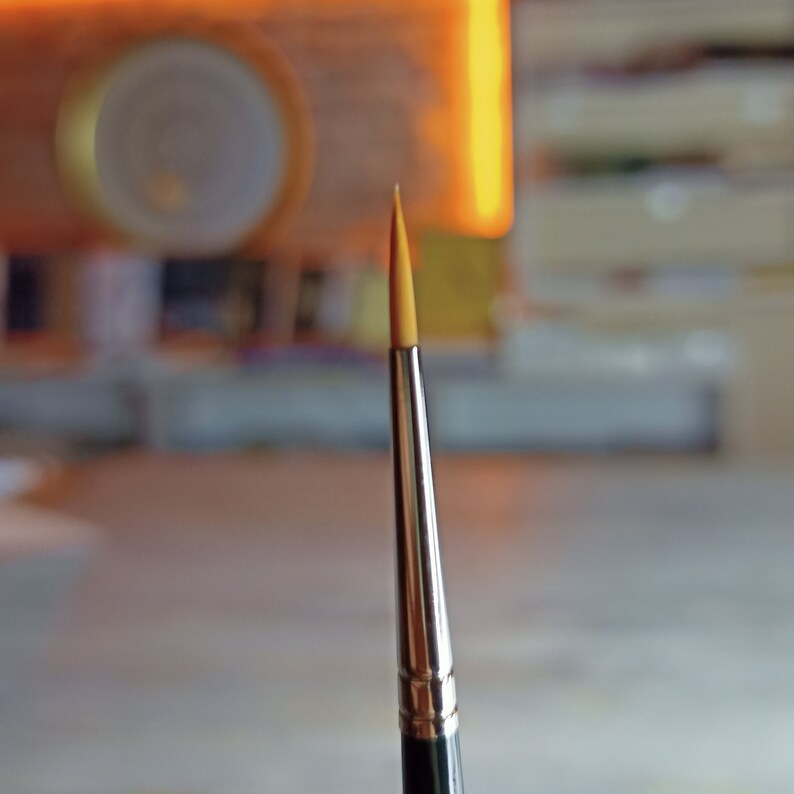 May include: A close-up of a paintbrush with a thin, pointed, yellow bristle tip and a silver metal handle.