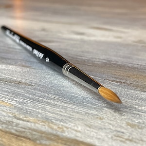 Może przedstawiać: Czarny i srebrny pędzel z okrągłą końcówką i drewnianym trzonkiem. Pędzel ma srebrną skuwkę i numer 5 wydrukowany na trzonku. Włosie jest jasnobrązowe i zwężone.