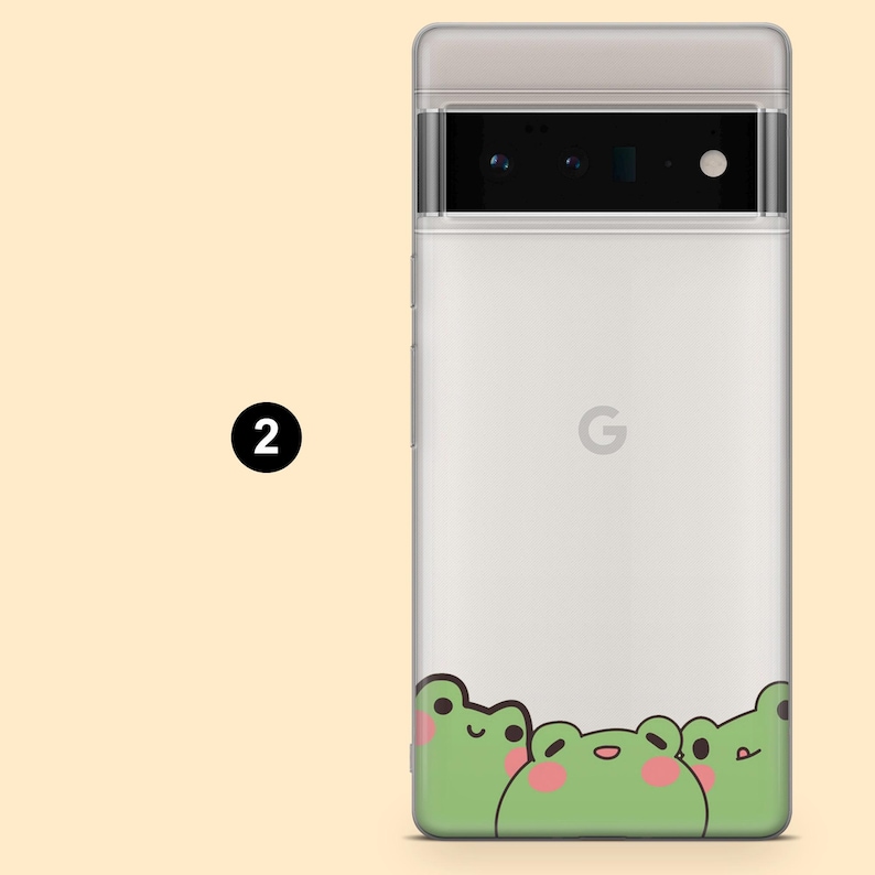 May include: A white phone case with a clear back and a design of three green frogs with pink cheeks at the bottom. The phone case has a black camera lens and the Google logo on the back.