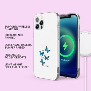 May include: A white phone case with a clear back. The case has a design of blue butterflies and the text "God is love 1 John 4:7-21". The phone is charging wirelessly on a white charging pad.