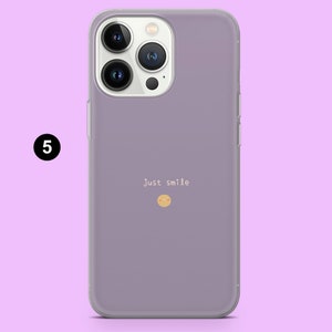 May include: A purple phone case with a clear back and a camera bump. The case has the text "Just smile" and a small smiley face printed on the back.
