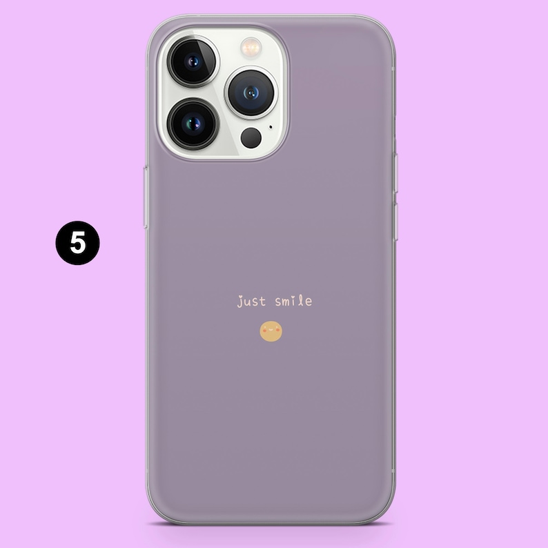 May include: A purple phone case with a clear back and a camera bump. The case has the text "Just smile" and a small smiley face printed on the back.