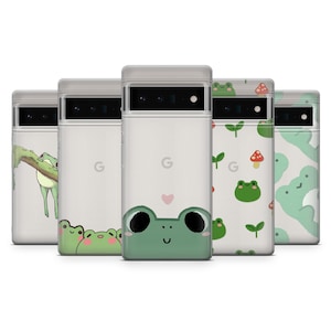 May include: Set of six clear phone cases with different frog designs. The cases have a white background and feature green frogs with black eyes and white accents. Some cases have a heart shape, while others have a frog on a branch or a mushroom.