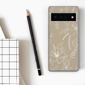May include: A beige phone case with a white floral design. The case has a cutout for the camera lens.