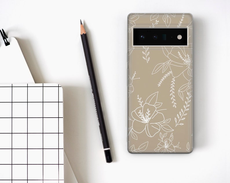 May include: A beige phone case with a white floral design. The case has a cutout for the camera lens.