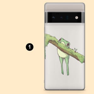 May include: A white phone case with a green frog hanging from a branch. The frog is holding onto the branch with its feet and has its eyes closed. The branch is covered in green moss.