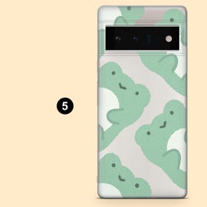 May include: A clear phone case with a white background and a pattern of green frogs. The case has a black camera lens cutout.