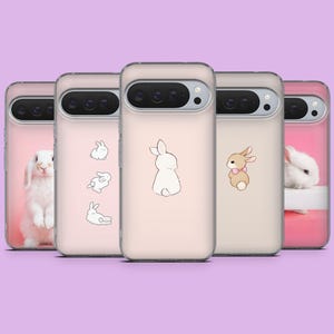 Puede incluir: Una colección de fundas para teléfonos con diseños de conejos. Las fundas presentan imágenes de conejos e ilustraciones de conejitos en varios estilos, incluyendo un conejo real y dibujos animados. Las fundas son en tonos de rosa y beige.