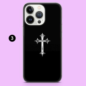 May include: A black phone case with a silver cross design. The case has a clear back and a black front with a silver cross in the center.