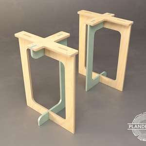Op de afbeelding: Twee houten krukjes met een lichte houtkleur en lichtblauwe accenten. De krukjes hebben een uniek ontwerp met een kruisvormige basis en een rechthoekig bovenblad.