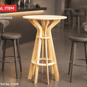 Puede incluir: Una mesa de bar de madera clara con una parte superior redonda y una base única de marco abierto, flanqueada por dos taburetes de bar de color gris oscuro. Los taburetes tienen respaldos curvos y reposapiés circulares. El texto "DIGITAL ITEM" y "FREE CUSTOM SIZE & THICKNESS" es visible.