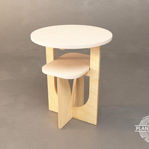 Może przedstawiać: Jasny drewniany stolik pomocniczy z białym blatem i dolną półką. Stolik ma unikalny design z wycięciami po bokach.