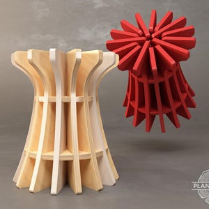 May include: A wooden stool with a unique, geometric design. The stool is made of light wood and has a white painted finish. The stool is shown next to a red, geometric object.