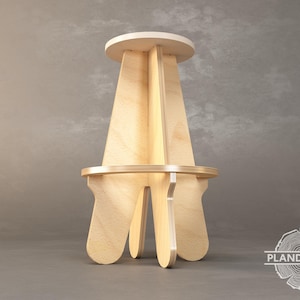 May include: A wooden stool with a simple, modern design. The stool has a circular seat and four legs that are shaped like a stylised flower.