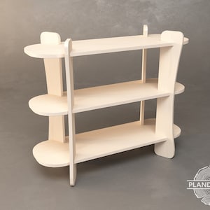 Op de afbeelding: Een drielaags, lichtgekleurd houten schap. De planken zijn ovaal van vorm en worden ondersteund door verticale en gebogen zijsteunen. Het ontwerp is minimalistisch en modern, geschikt voor het uitstallen van items. De unit is gemaakt van onbewerkt hout.