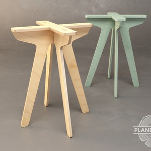 Op de afbeelding: Twee houten tafels met drie poten, een in naturel hout en een in lichtgroen. De tafels hebben een vierkant blad en een eenvoudig, modern ontwerp.