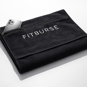 May include: Black towel with a zippered pocket, holding a silver smartphone. The word "FITBURSE" is embroidered in white across the front. The towel is folded neatly on a white surface.