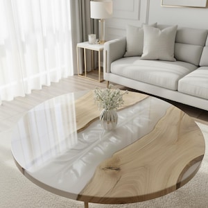 May include: A round coffee table with a wood and white resin top. The table has a natural wood grain pattern on the edges and a glossy white resin center. A small vase of white flowers sits on the table.